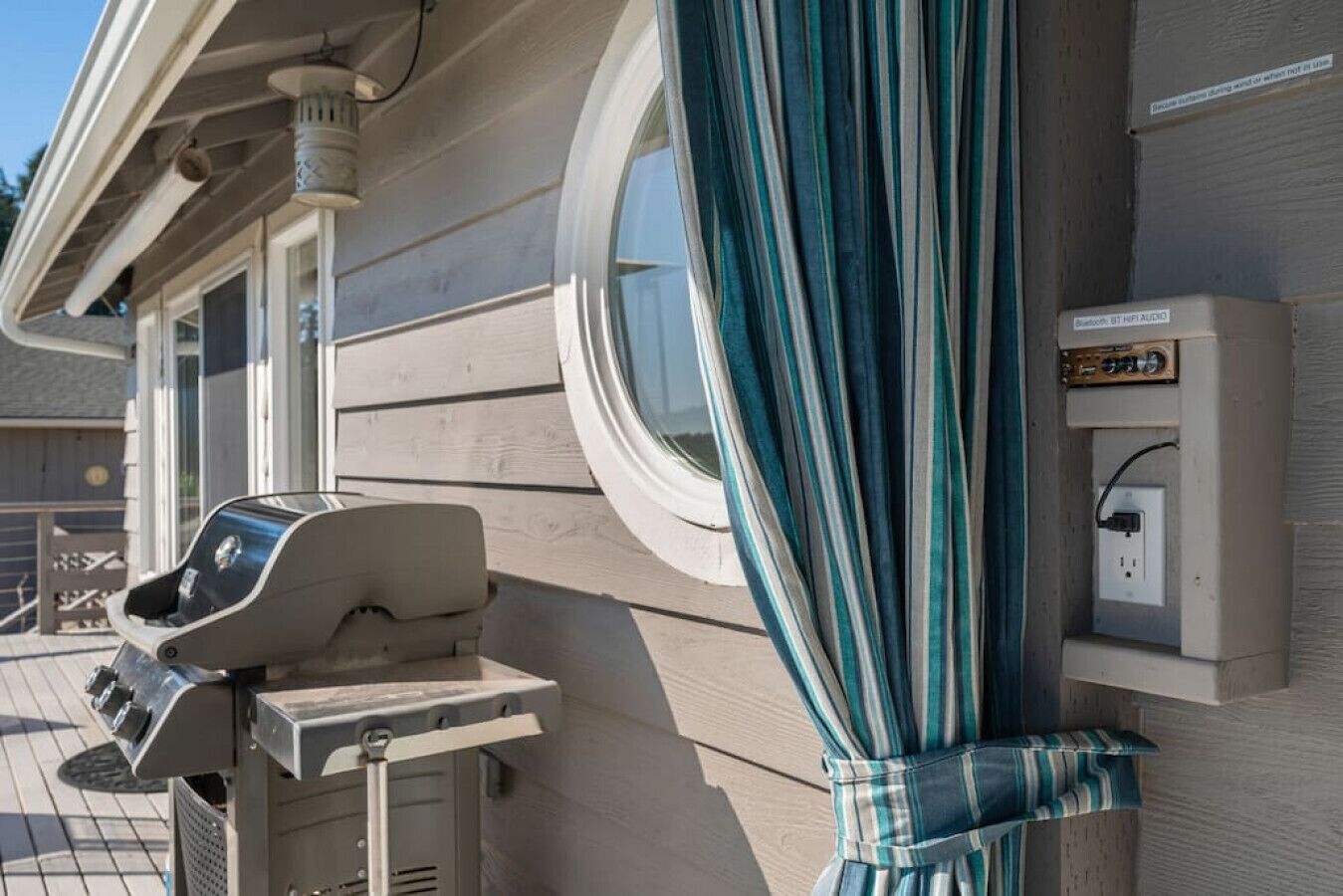 Une terrasse avec un barbecue, une prise de courant et une fenêtre avec des rideaux.
