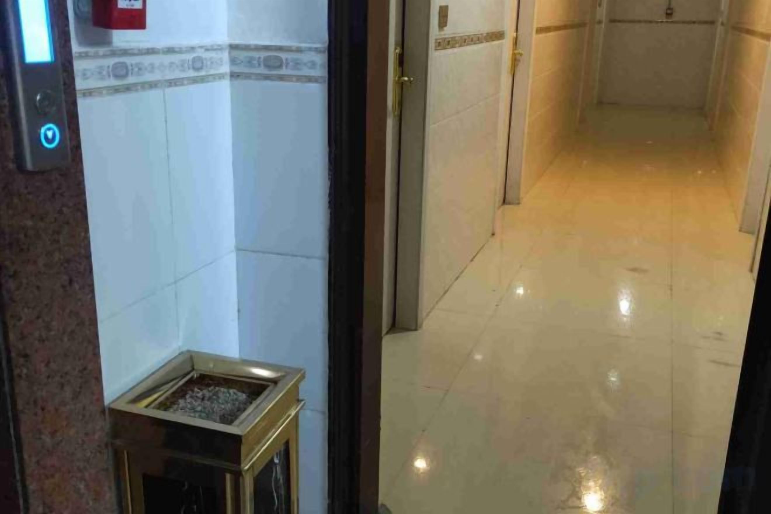 A corridor with a tiled wall and a small trash bin on the left.