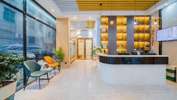 Una moderna zona de recepción de hotel con un mostrador curvo, área de asientos con sillas y un amplio ventanal con vista a coches estacionados afuera.
