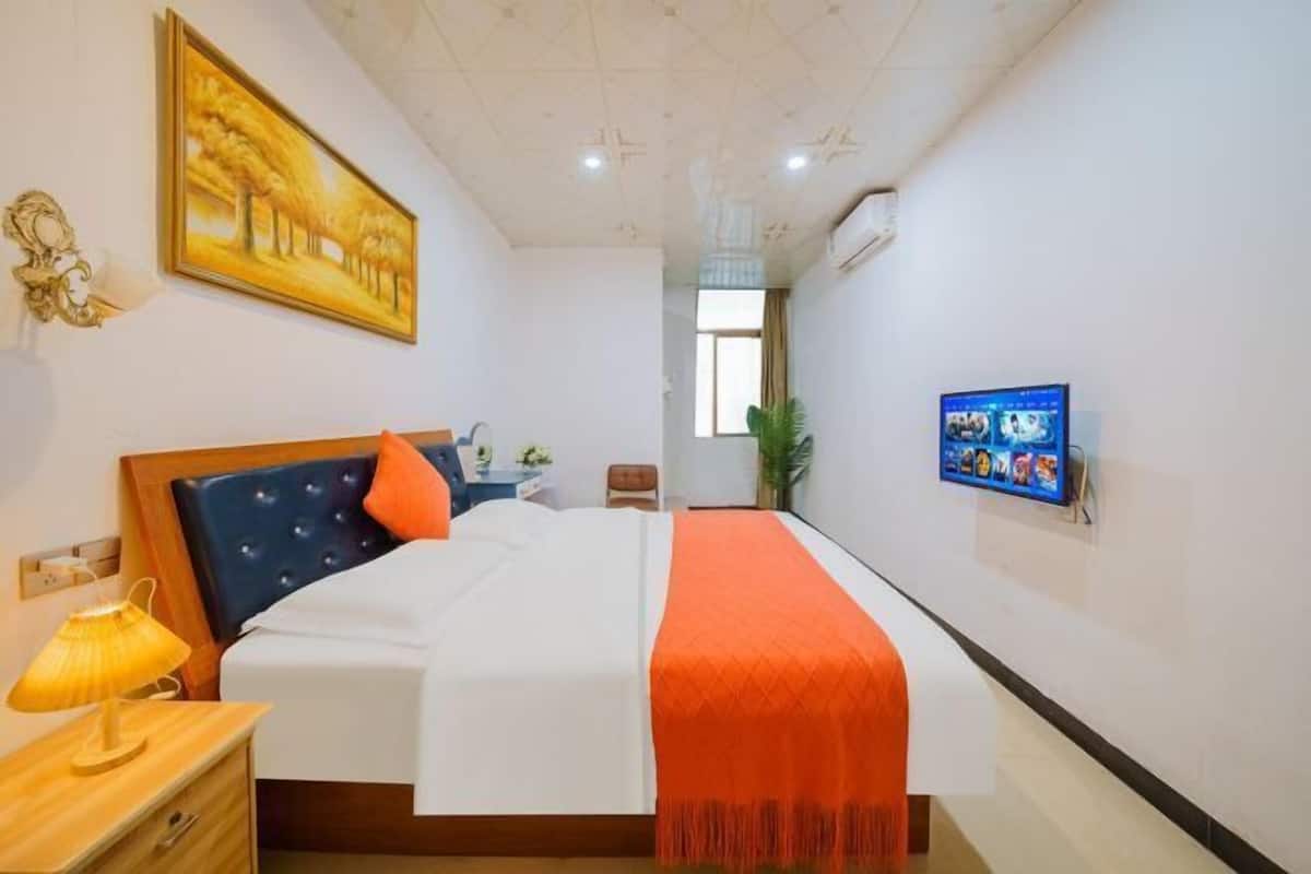 A hotel room with a bed, a TV mounted on the wall, a painting on the wall, and a window.