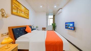 A hotel room with a bed, a TV mounted on the wall, a painting on the wall, and a window.