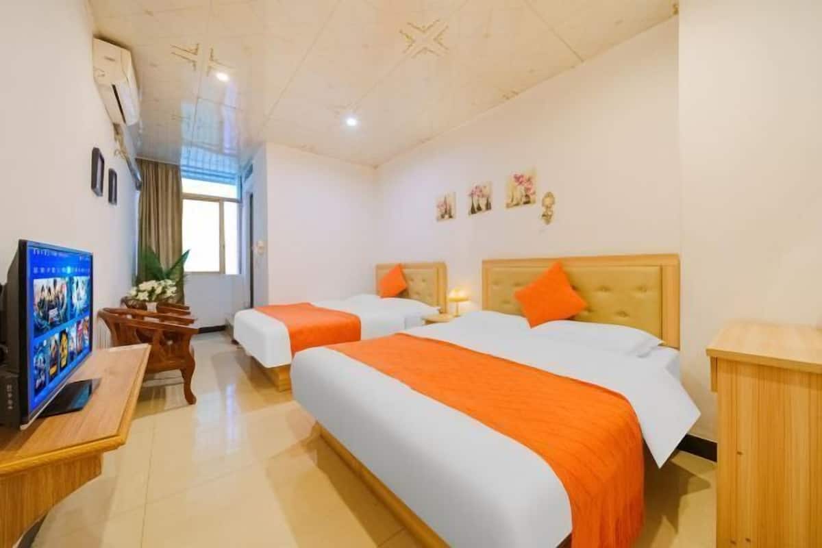 A hotel room with two beds, a TV, a desk, and a window.
