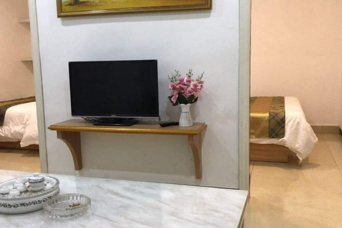 A room with a television on a wooden stand, a vase with flowers, and a marble table with a tray of items.