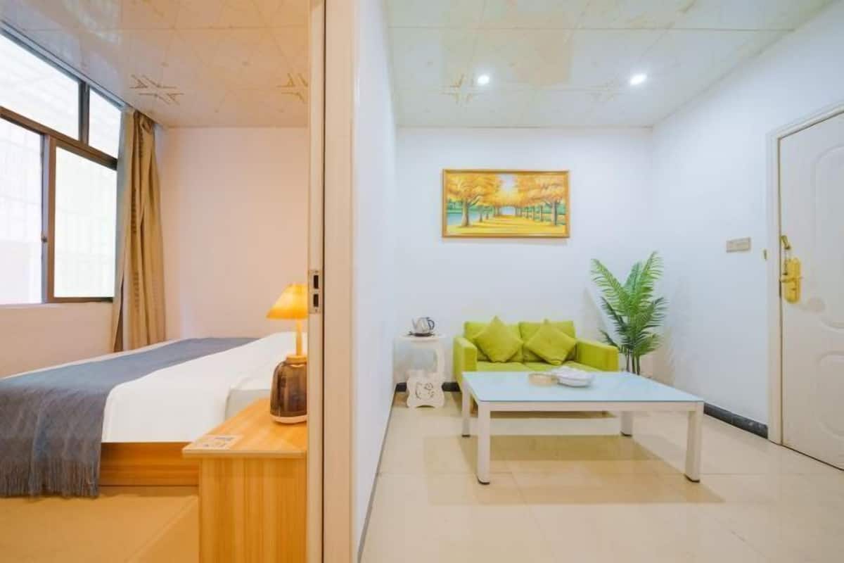 A hotel room with a bed, a small table, a green sofa, a painting on the wall, and a door.