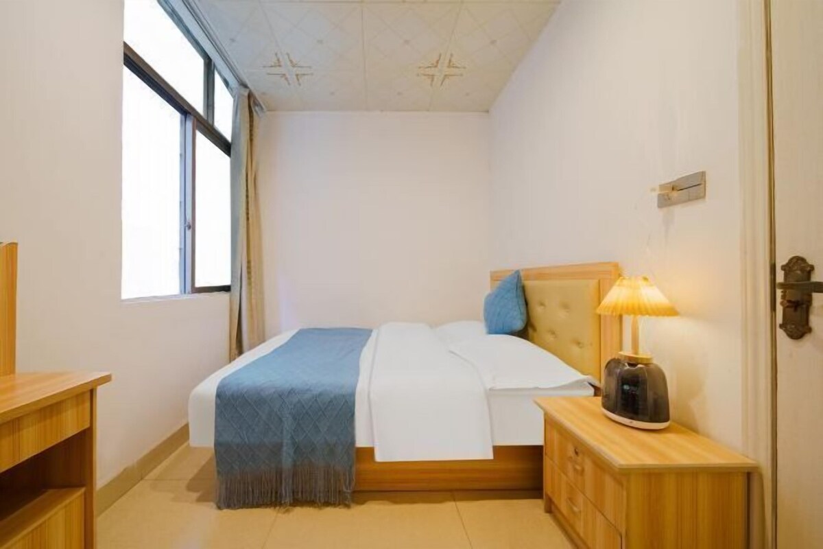 A bedroom with a bed, bedside table, lamp, and a window.