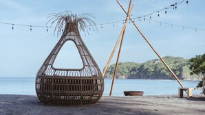 Eine Strandkulisse mit einem Korbstuhl, Lichterketten und einer Holzkonstruktion.