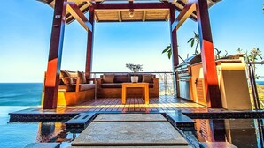 Ein überdachter Außenbereich mit Meerblick, ausgestattet mit einer Holzkonstruktion und einem Pool.