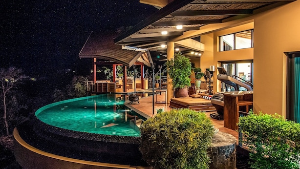 Ein Nachtblick auf ein Resort mit Schwimmbad, Außenbereich zum Sitzen und einem überdachten Bereich mit Fitnessgeräten.