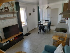 A modern living room with a flat-screen TV, a sofa, and a dining area with a table and chairs.