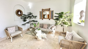 A modern living room with a glass coffee table, wicker furniture, a large mirror, and potted plants. - Unique Moroccan Style Villa in Golf Beach Resort (Punta Cana)