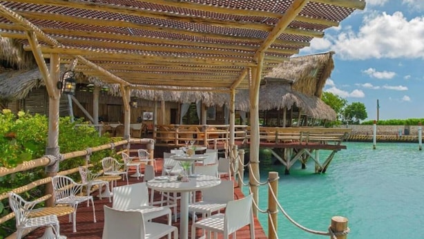 A seaside restaurant with outdoor seating, a thatched roof, and a view of the water. - Unique Moroccan Style Villa in Golf Beach Resort (Punta Cana)