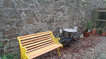 A wooden bench with yellow metal armrests, a small round table with a white top, and potted plants.