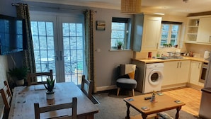 A compact living space with a dining area, a sofa, a washing machine, and a kitchen area. - Ground Floor Bodmin Retreat Free Parking (Bodmin)