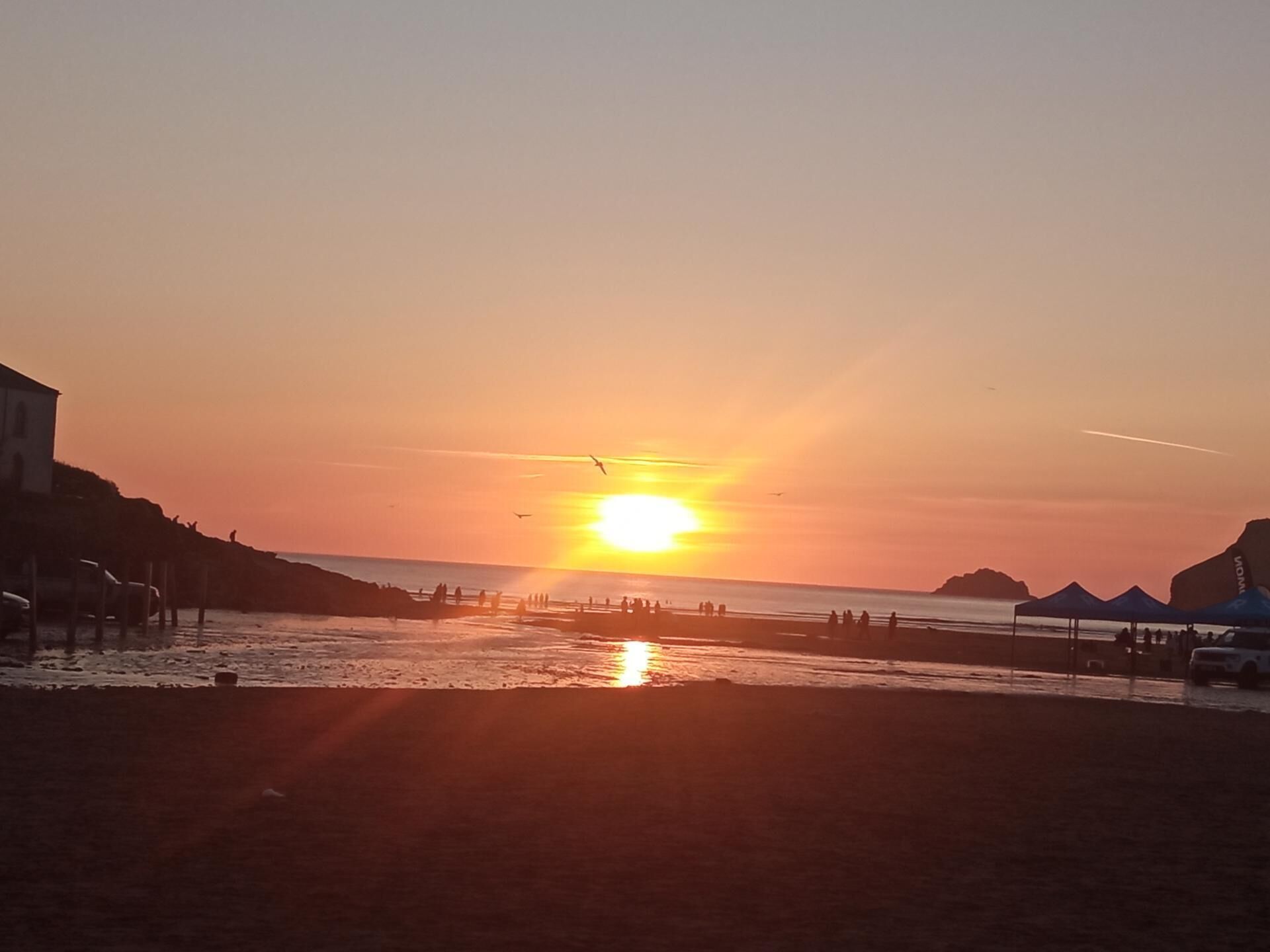 Un coucher de soleil sur une plage, avec des personnes et des tentes.
