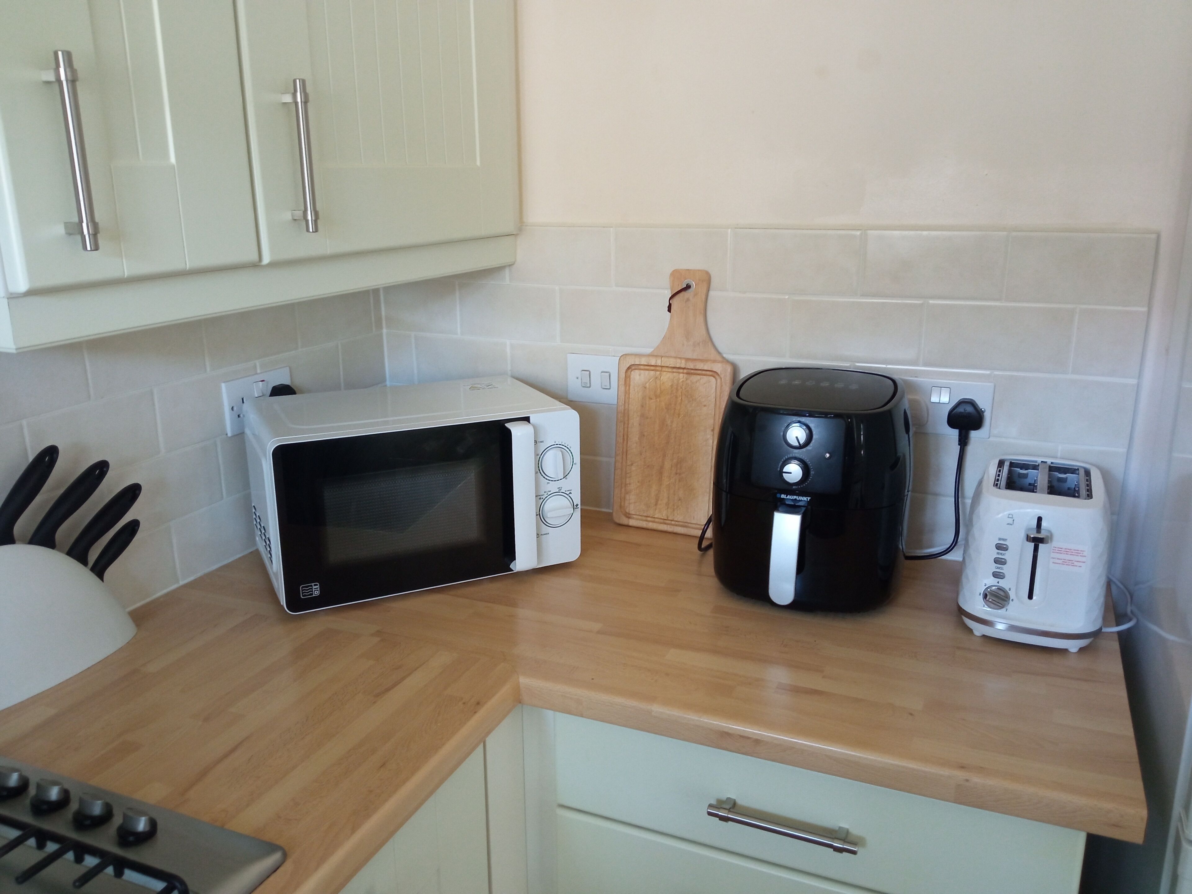 A kitchen with a microwave, toaster, and air fryer on the counter, a wooden cutting board, and a gas stove.