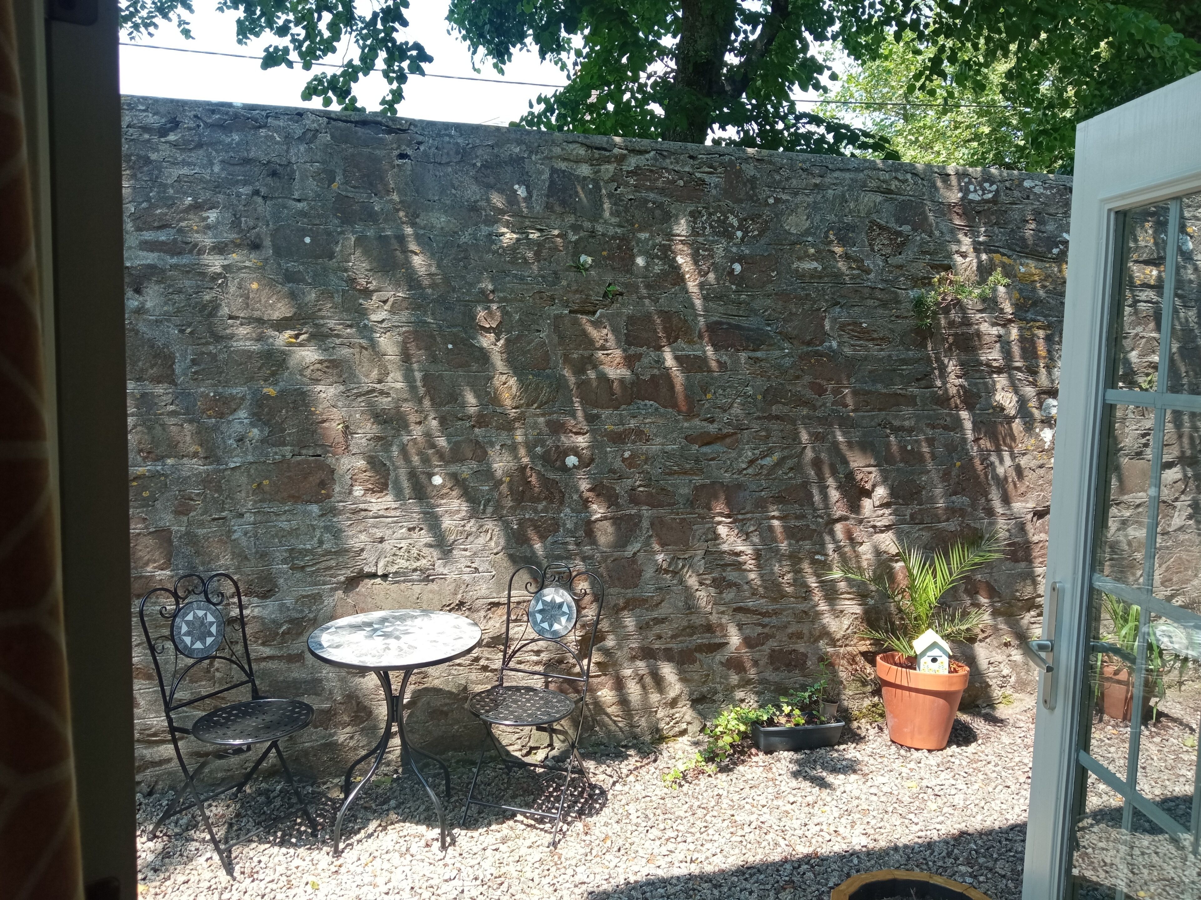 A stone wall, two metal tables with chairs, and potted plants in a courtyard.