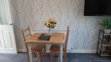 A dining area with a table, chairs, a vase with sunflowers, a black folder, and a TV on the wall.