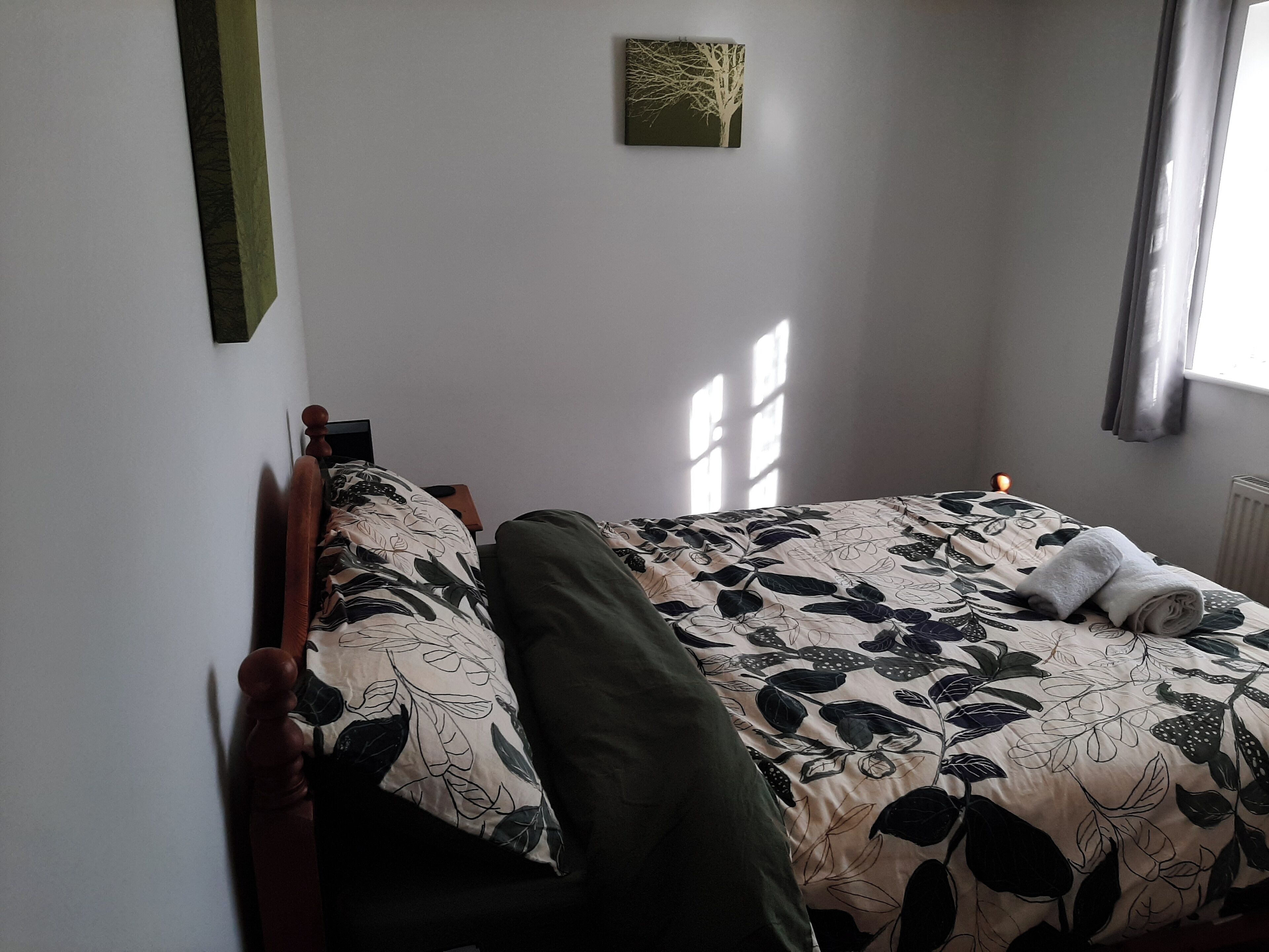 A bedroom with a bed, a nightstand, a bedside table, a lamp, and a window with curtains.