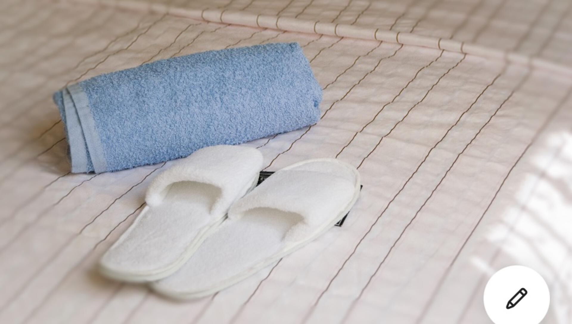 A pair of white slippers and a blue towel on a tiled floor.