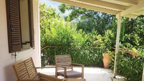 An outdoor seating area with two wooden chairs and a table, surrounded by greenery and a potted plant. - Villa Delphia One Bedroom Traditional House (Kefalonia)