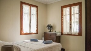 A bedroom with two windows, a bed, a nightstand, and a fan. - Villa Delphia One Bedroom Traditional House (Kefalonia)