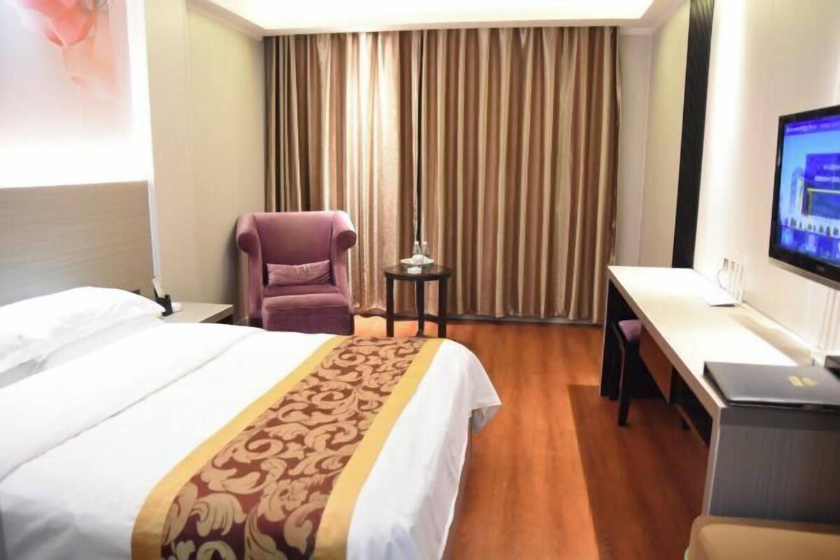 Una habitación de hotel con cama, escritorio, silla, televisor y cortina.