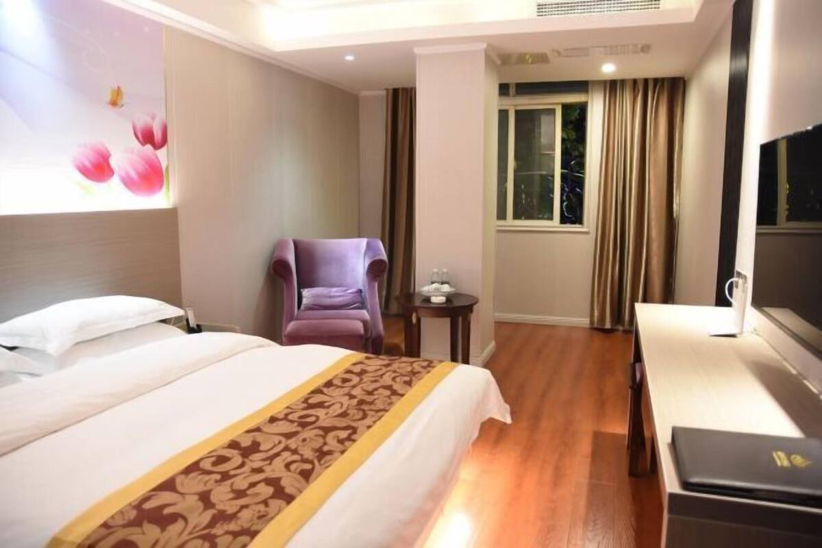 Habitación de hotel con cama, una silla, una mesita, televisor y ventana con cortinas.