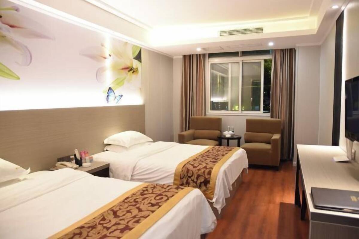 Habitación de hotel con dos camas, un escritorio, una silla, un televisor y una ventana con cortinas.