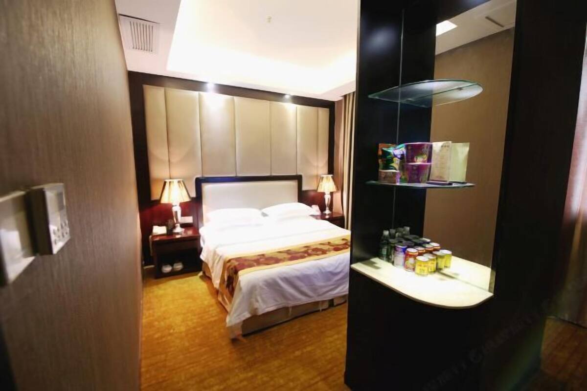 Una habitación de hotel con cama, lámparas de noche, mesita de noche, espejo y estante con artículos de aseo.