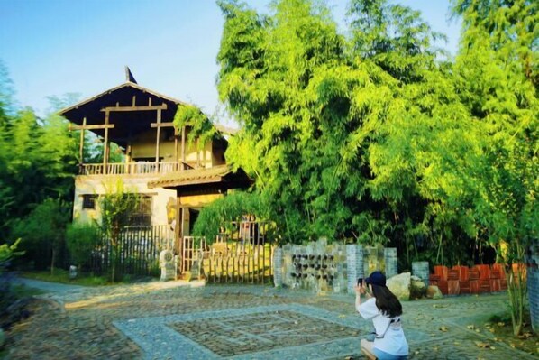 A traditional wooden house with a balcony, surrounded by lush greenery and a stone pathway. - Huaqitang Rural Life Hostel (Wuhan)