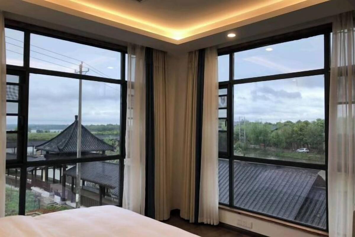 Une chambre d’hôtel dotée de grandes fenêtres, d’un lit et offrant une vue sur une architecture traditionnelle.