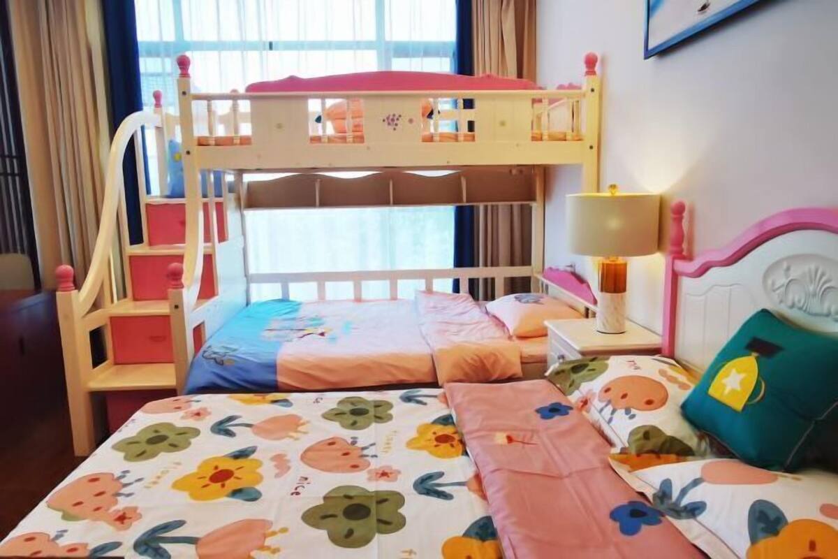 Une chambre d’enfant avec des lits superposés, une table de chevet avec une lampe et une couverture de lit aux motifs floraux et aux couleurs vives.