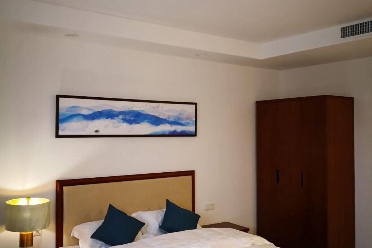 A hotel room with a bed, a wooden wardrobe, and a framed picture on the wall.