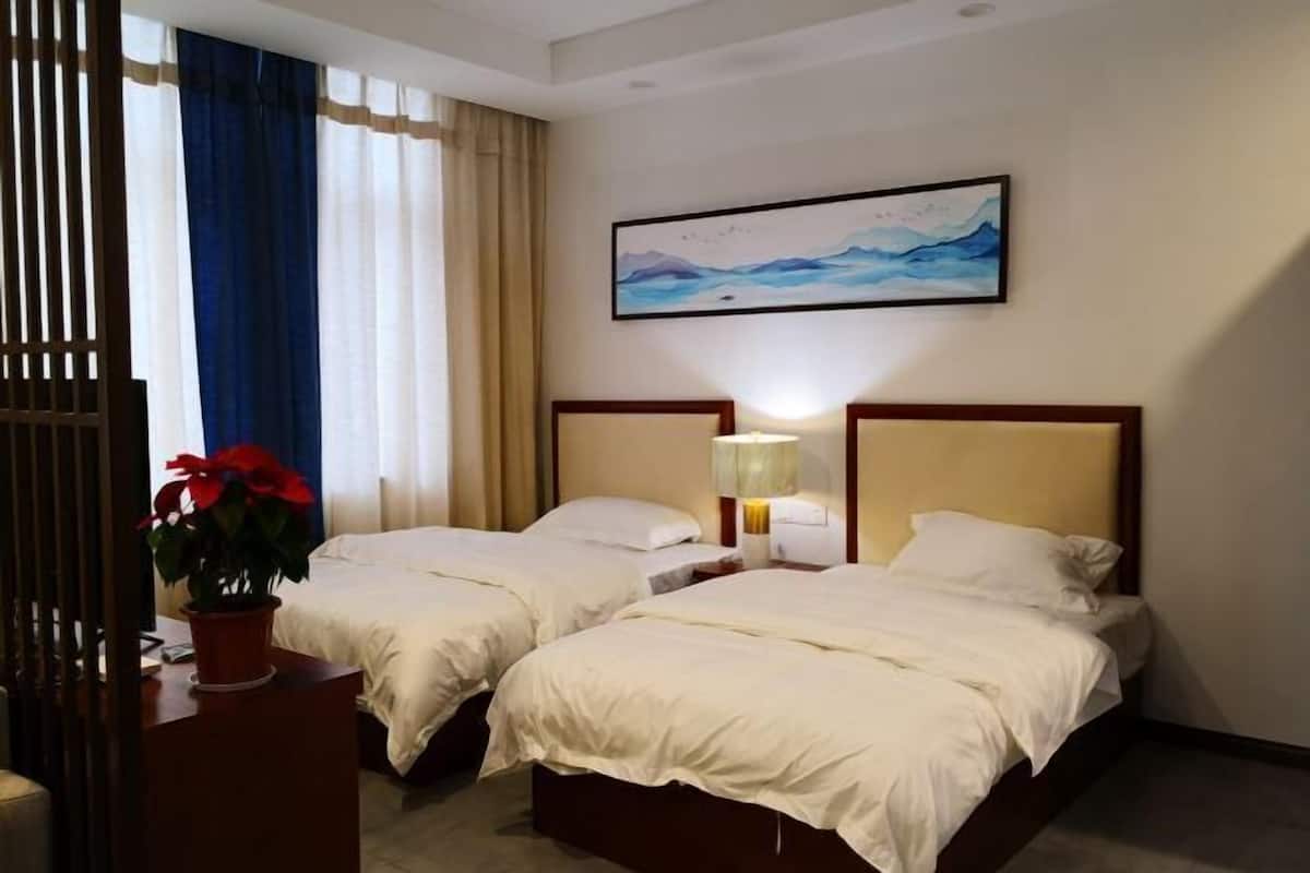 Une chambre d’hôtel avec deux lits, une table de chevet avec une lampe, une plante en pot et un tableau au mur.