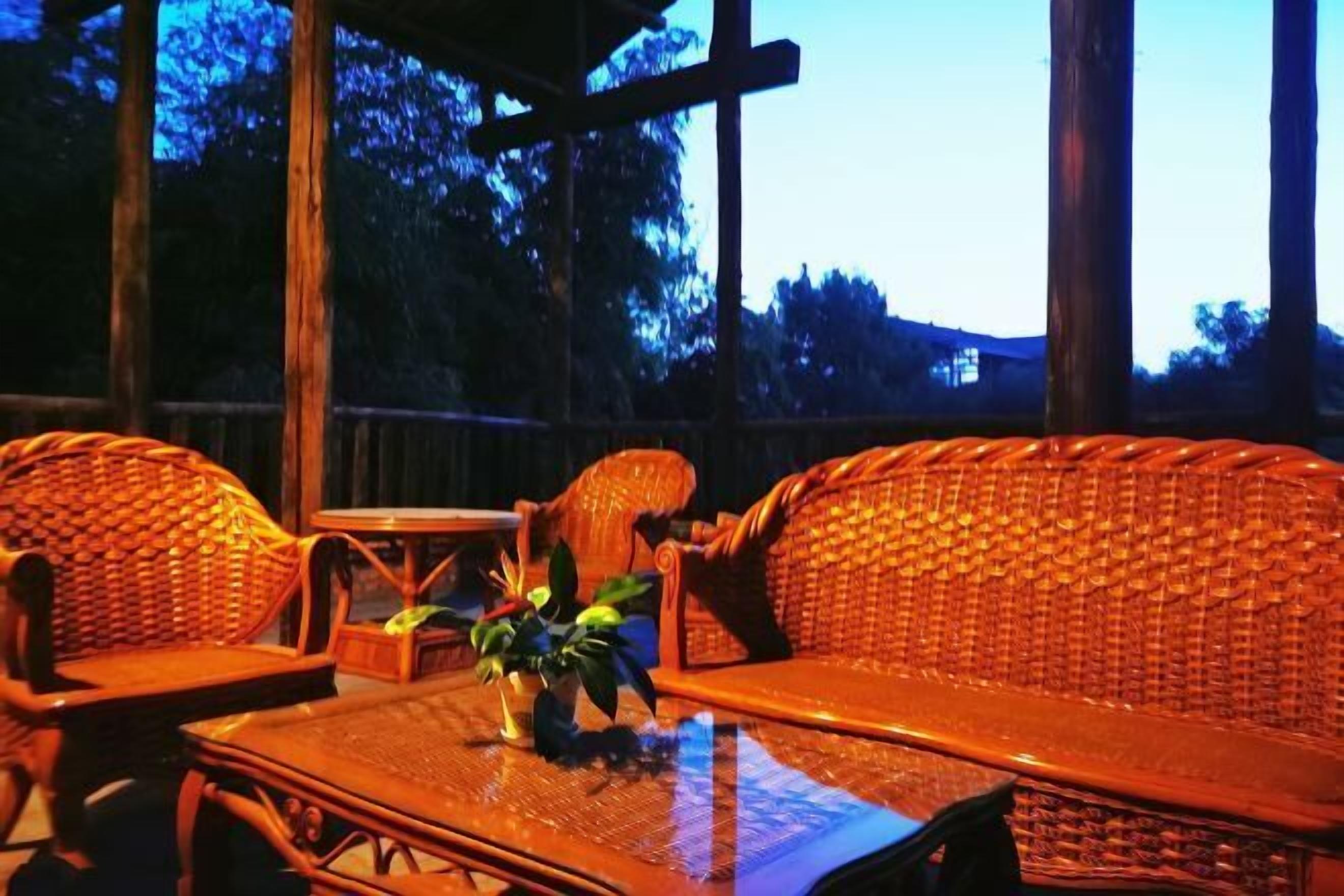 A wicker sofa and table set in a covered outdoor area with a view of trees and a building in the background.