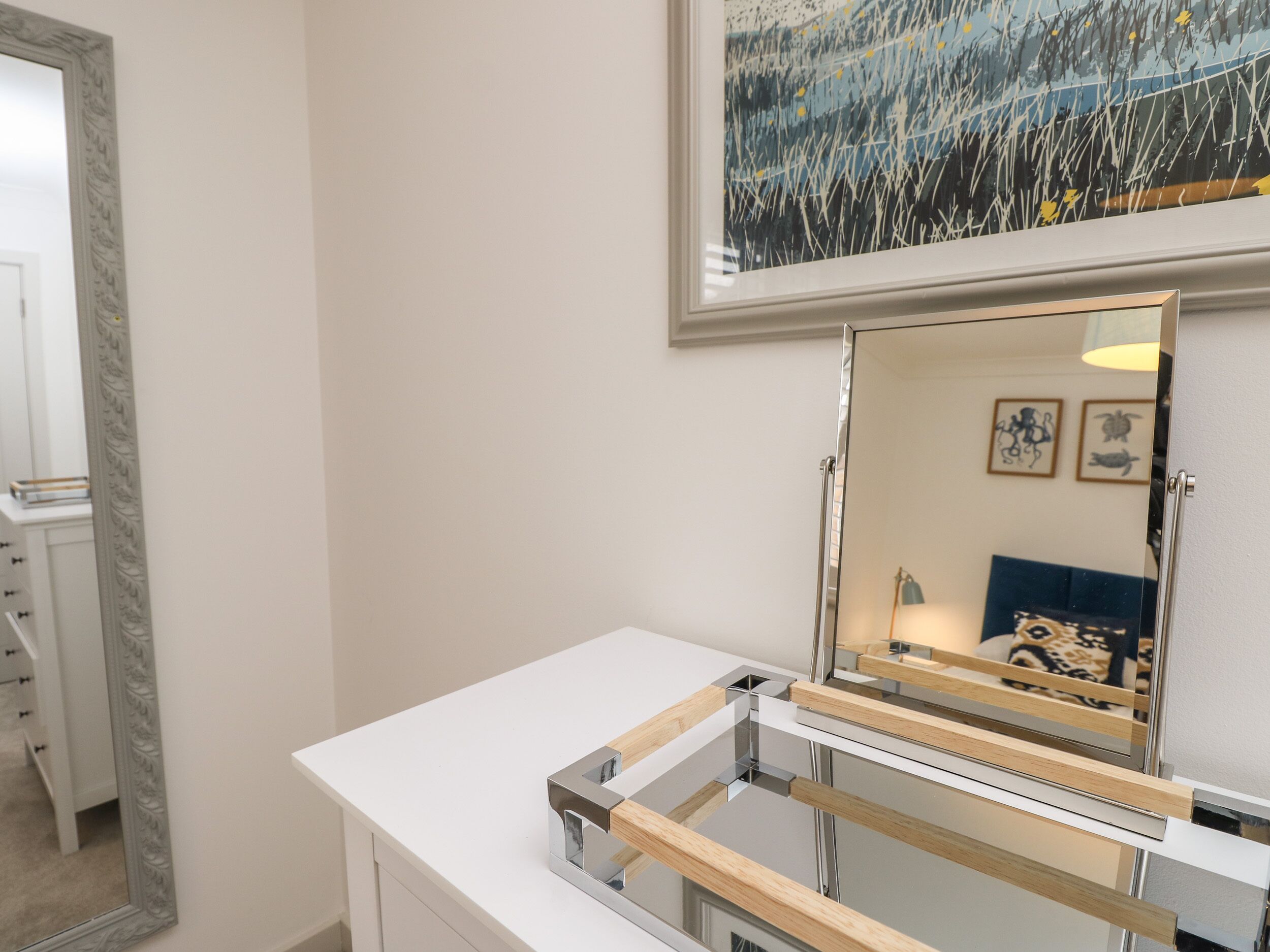 Un baño moderno con un tocador blanco, un espejo grande y una obra de arte enmarcada en la pared.