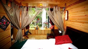 A cozy wooden cabin room with a bed, curtains, and a view of the outdoors. - Wuming Inn (Dali City)
