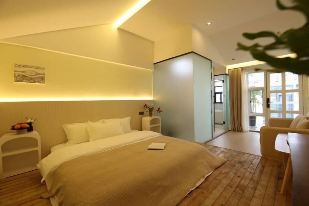 A modern hotel room with a large bed, a seating area, and a view of the outdoors.