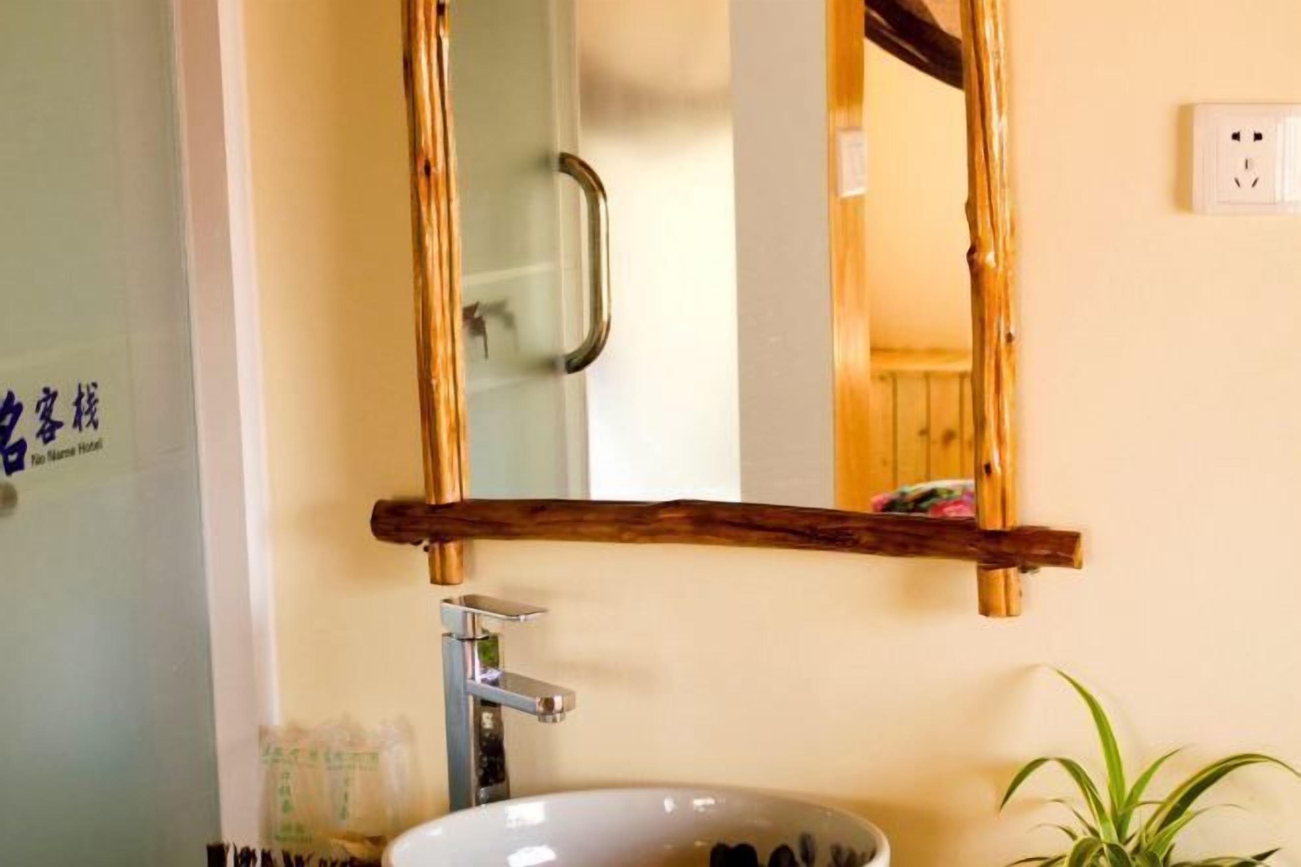 A bathroom with a wooden shelf above a sink, a mirror, and a potted plant.