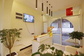 Zona de recepción con mostrador, televisor montado en la pared y un gran ventanal con vistas al exterior.