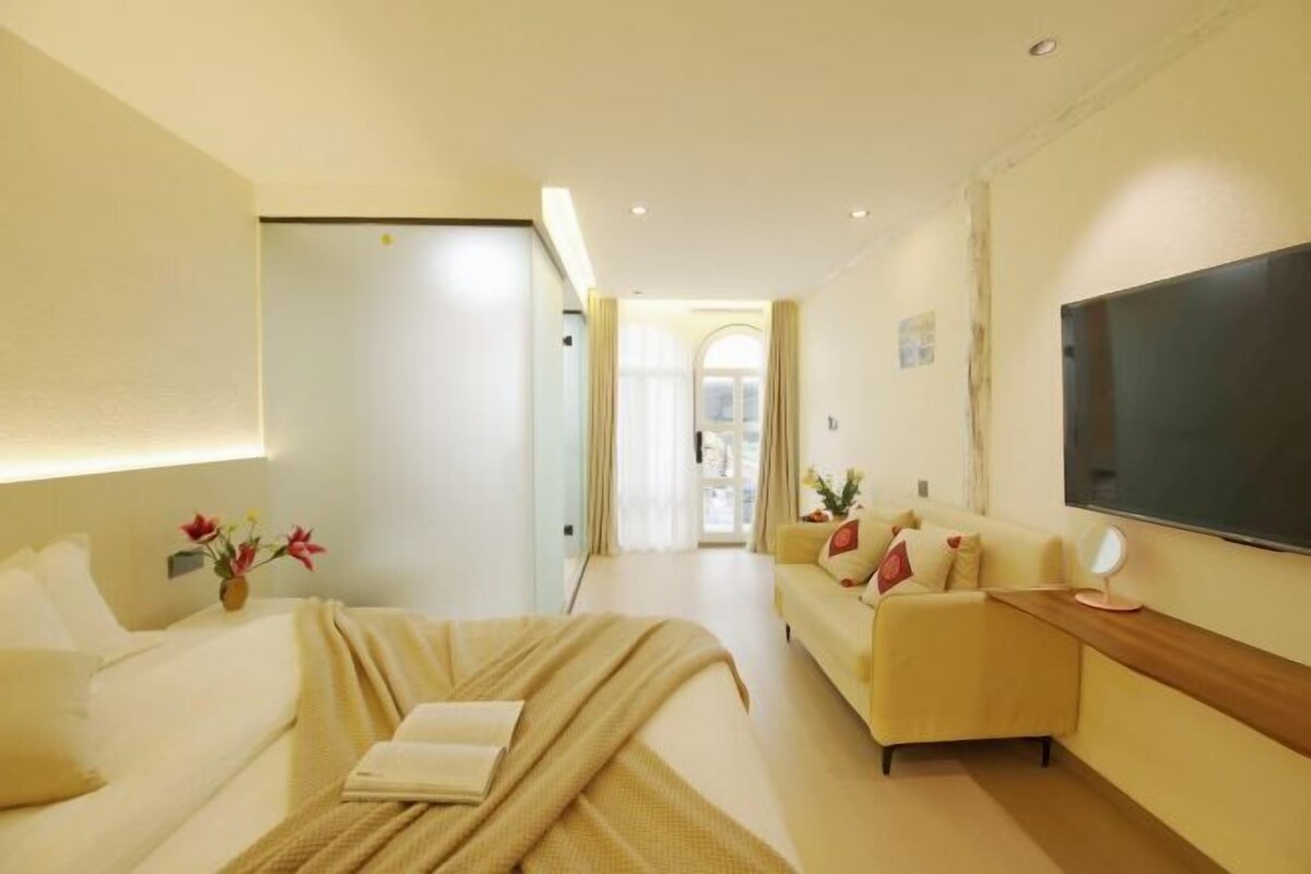 A hotel room with a bed, a sofa, a TV, and a large window.