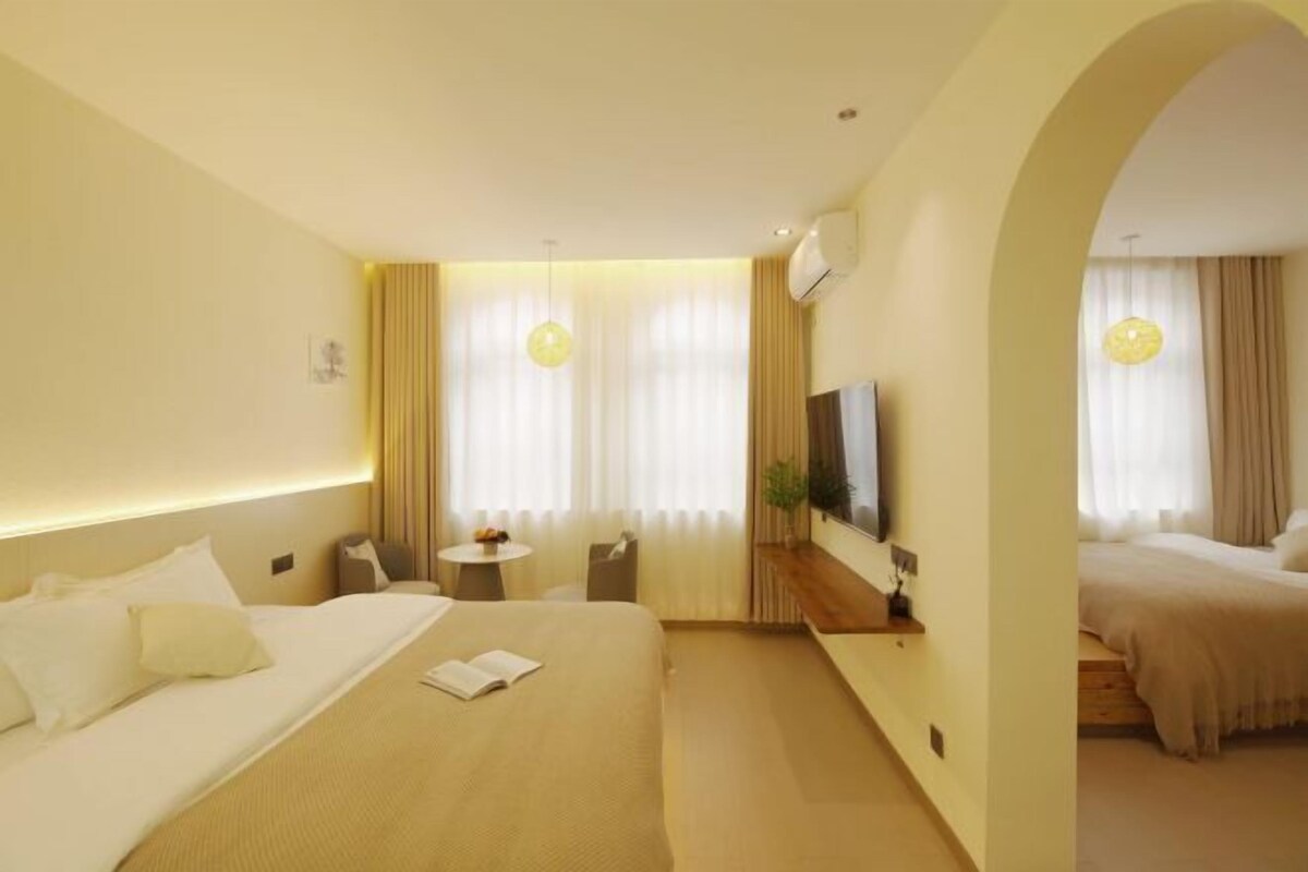 A hotel room with a large bed, a small table, a TV, and a seating area with curtains.