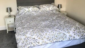 A bedroom with a dark headboard, a patterned bedspread, two bedside tables with lamps, and a carpeted floor. - Blacklaines Annexe Birdlip - Pet Friendly! (Gloucester)
