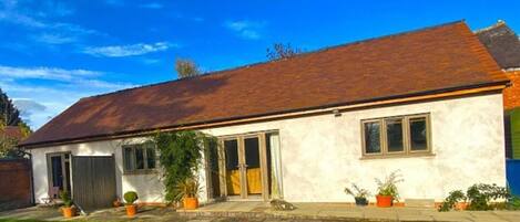 A single-story house with a sloped roof, a front door, and a garage door. There are potted plants in the front yard.