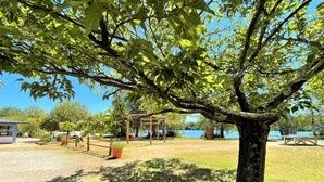 A park with a large tree, picnic tables, a wooden pergola, and a view of a lake. - Vacation rental near Royan in a magnificent setting (sainte gemme)