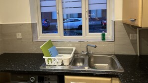 A kitchen with a window, a dish rack, a sink, and a dishwasher. - Entire Captivating 2-bed House in Manchester (Manchester)