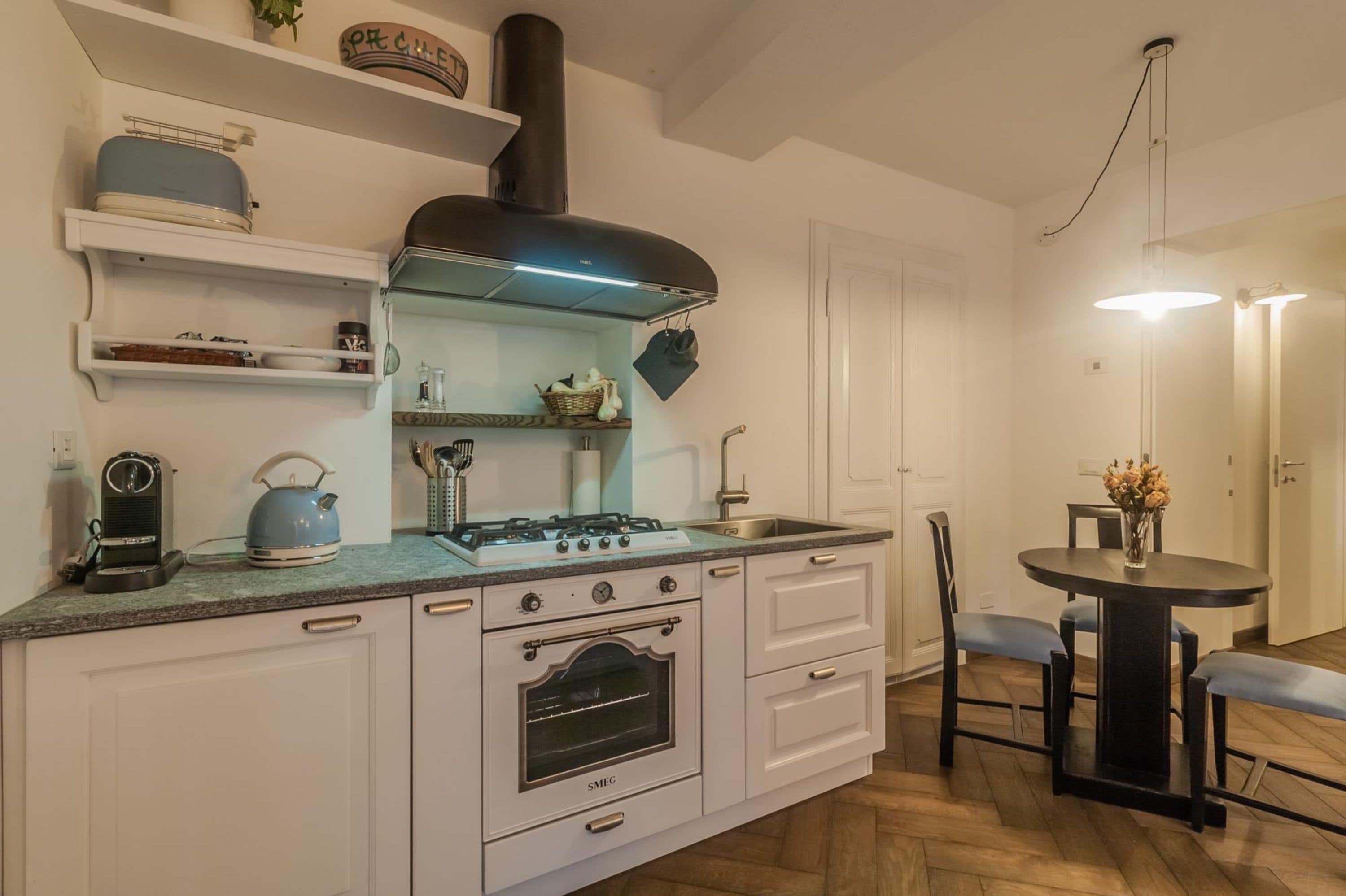 Une cuisine compacte avec des meubles blancs, un four encastré, une cuisinière à gaz et un petit coin repas comprenant une table ronde et des chaises.