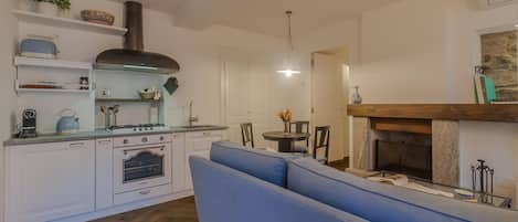 A compact kitchen with white cabinets, a blue sofa, and a fireplace.