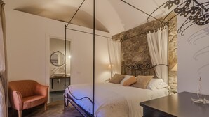 Een slaapkamer met een hemelbed, een accentmuur van steen, een houten vloer, een nachtkastje en een stoel.