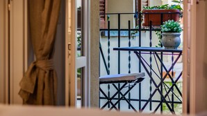 Een balkon met een kleine tafel en stoelen, planten in potten en uitzicht op de straat.